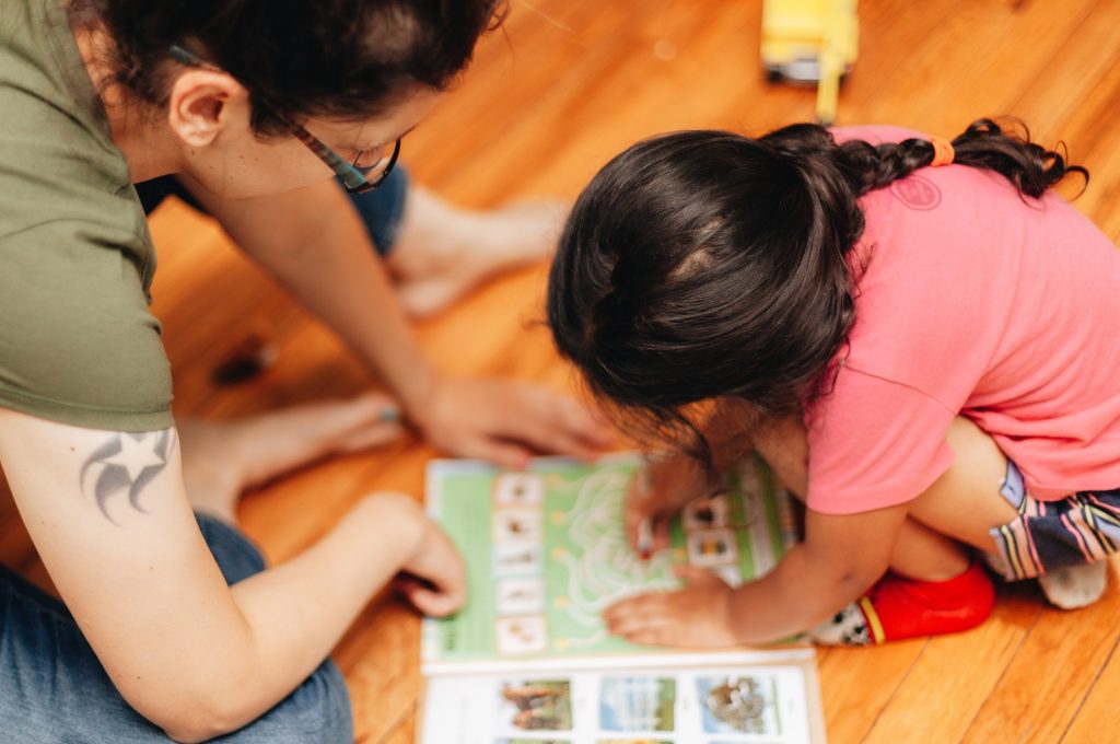 Mother and diverse daughter at home playing a game from a book, bonding, early education
